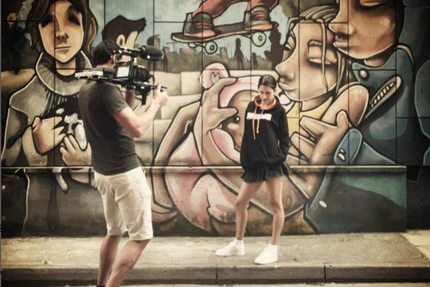 Person filming female model against a graffiti-covered wall wearing behave clobber hoodie